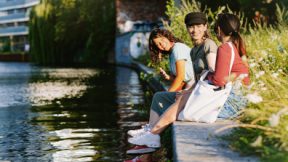 Trois étudiants sont assis au bord d'une rivière dans une ville et discutent.